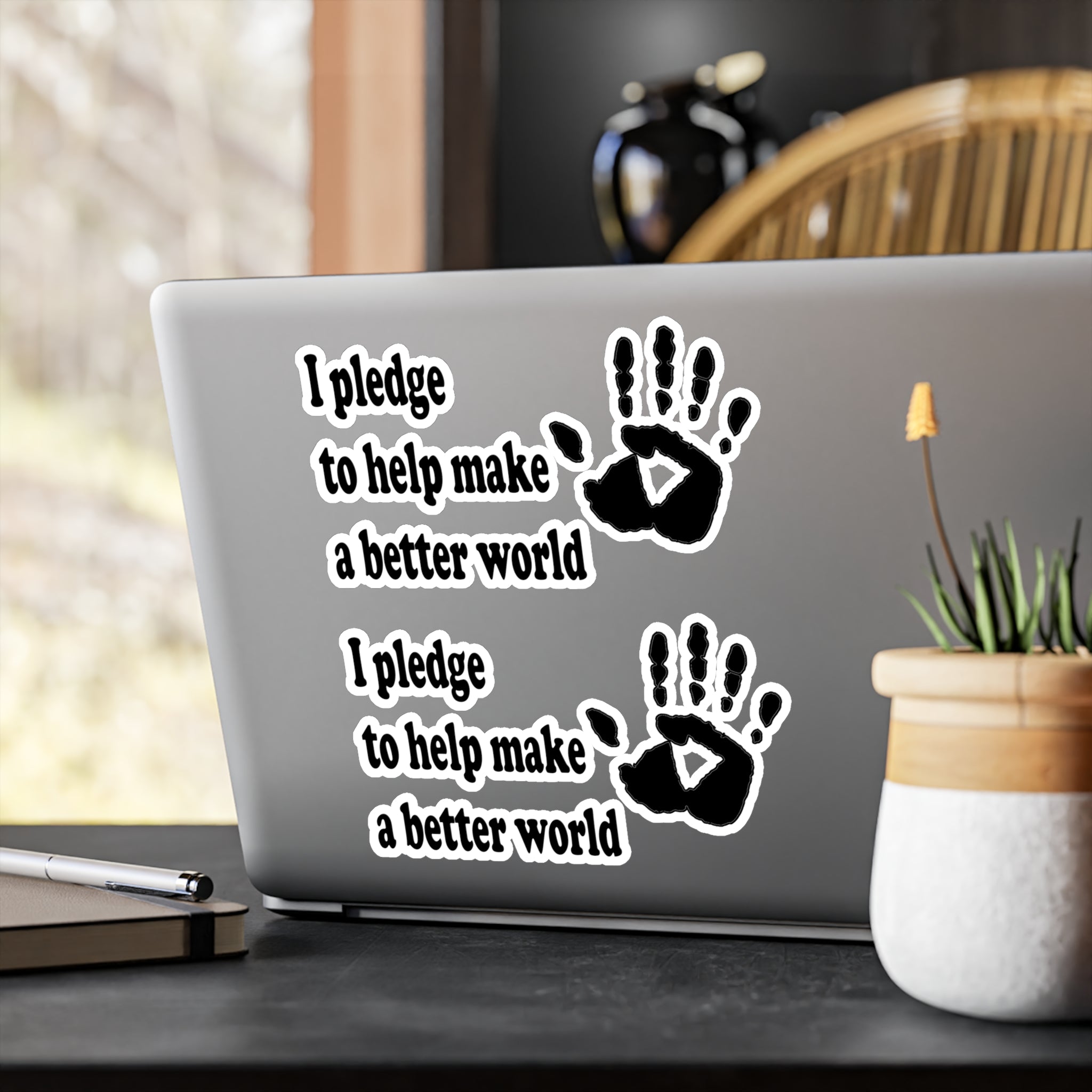 Laptop with 'I pledge to help make a better world' text and handprints on a desk.