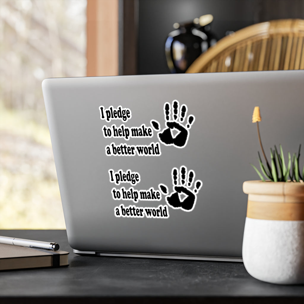 Laptop with stickers on it that has a handprint and says 'I pledge to help make a better world' on a desk with a plant and pen.