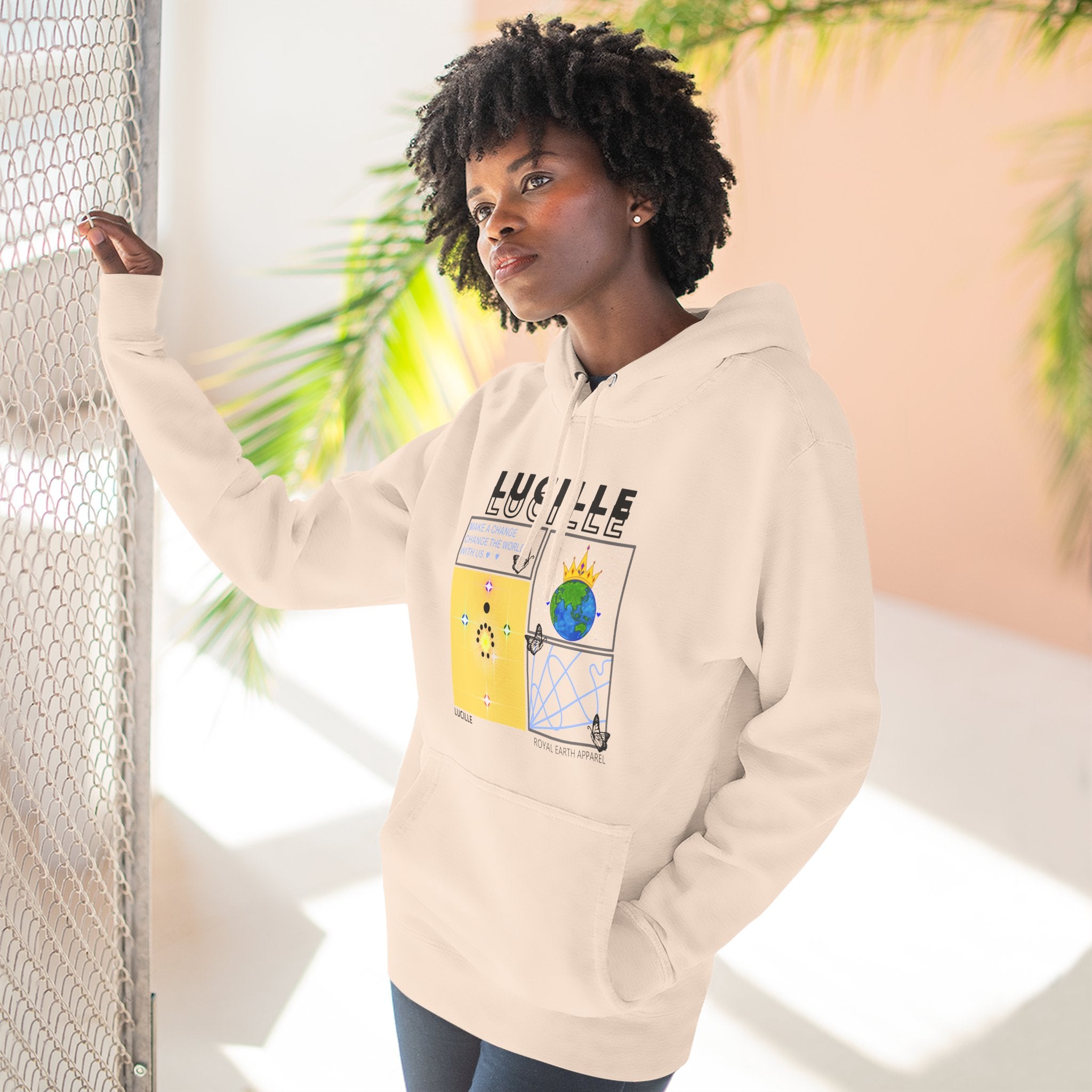 Person wearing a beige hoodie with a graphic design, standing against a light background with plants.