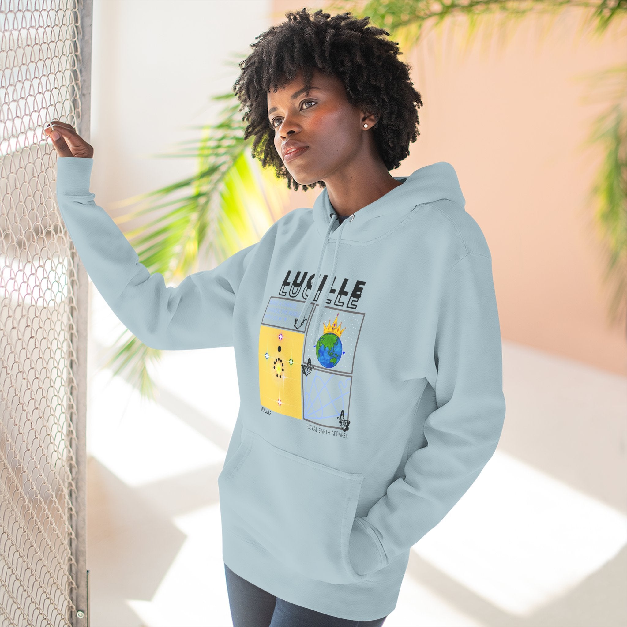 Person wearing a light blue hoodie with a Lucille graphic design and text, standing indoors with plants in the background.